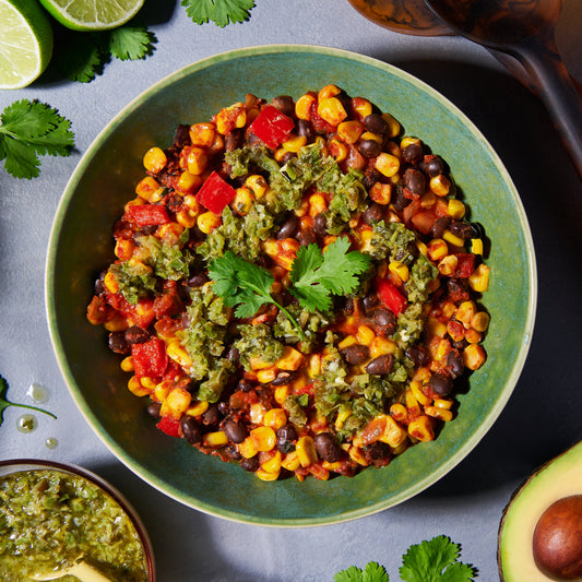 Overhead view of black beans with roast corn, red capsicum and jalapeño-lime salsa in a green bowl.