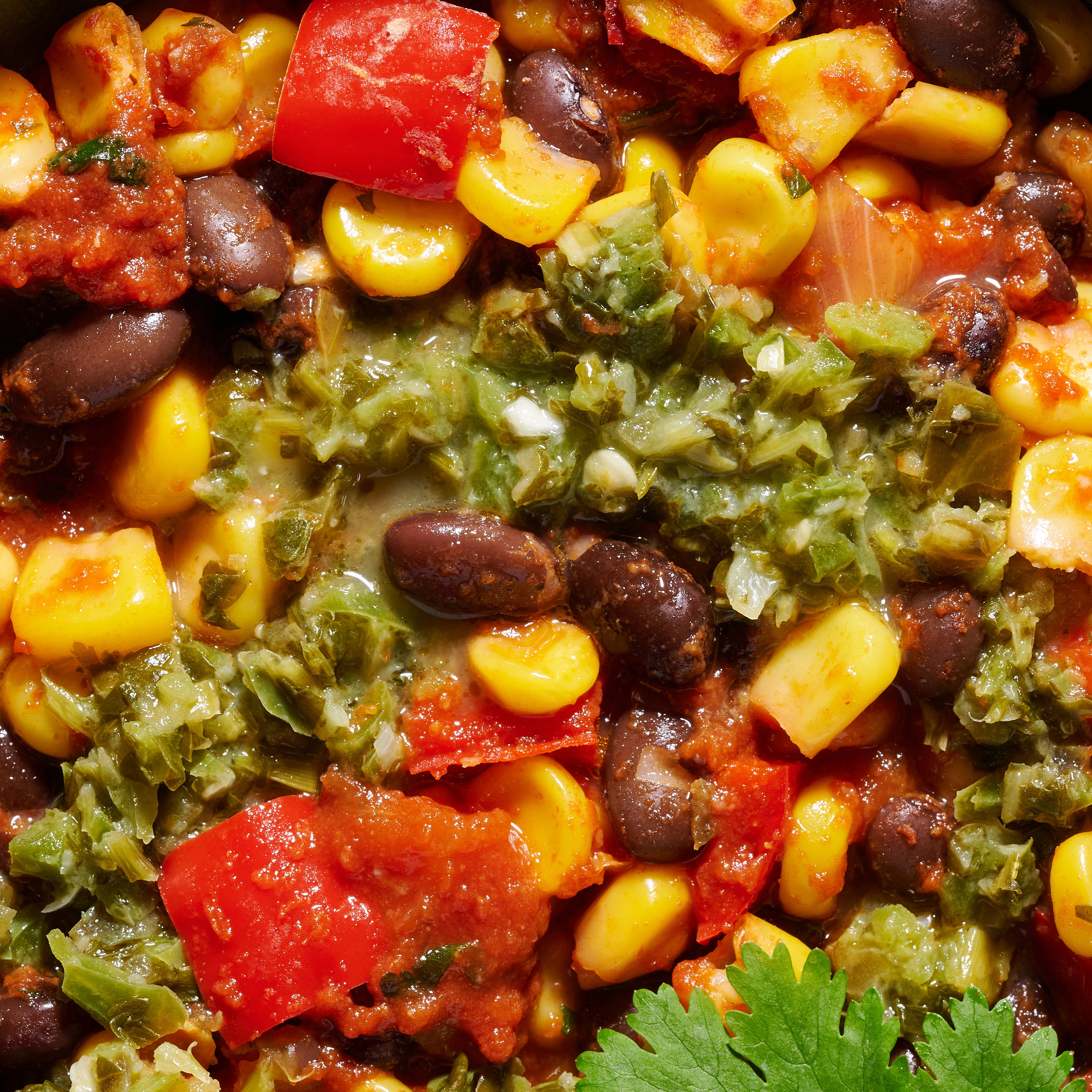 Close-up of black beans with roasted corn, red capsicum and jalapeño-lime salsa garnish.