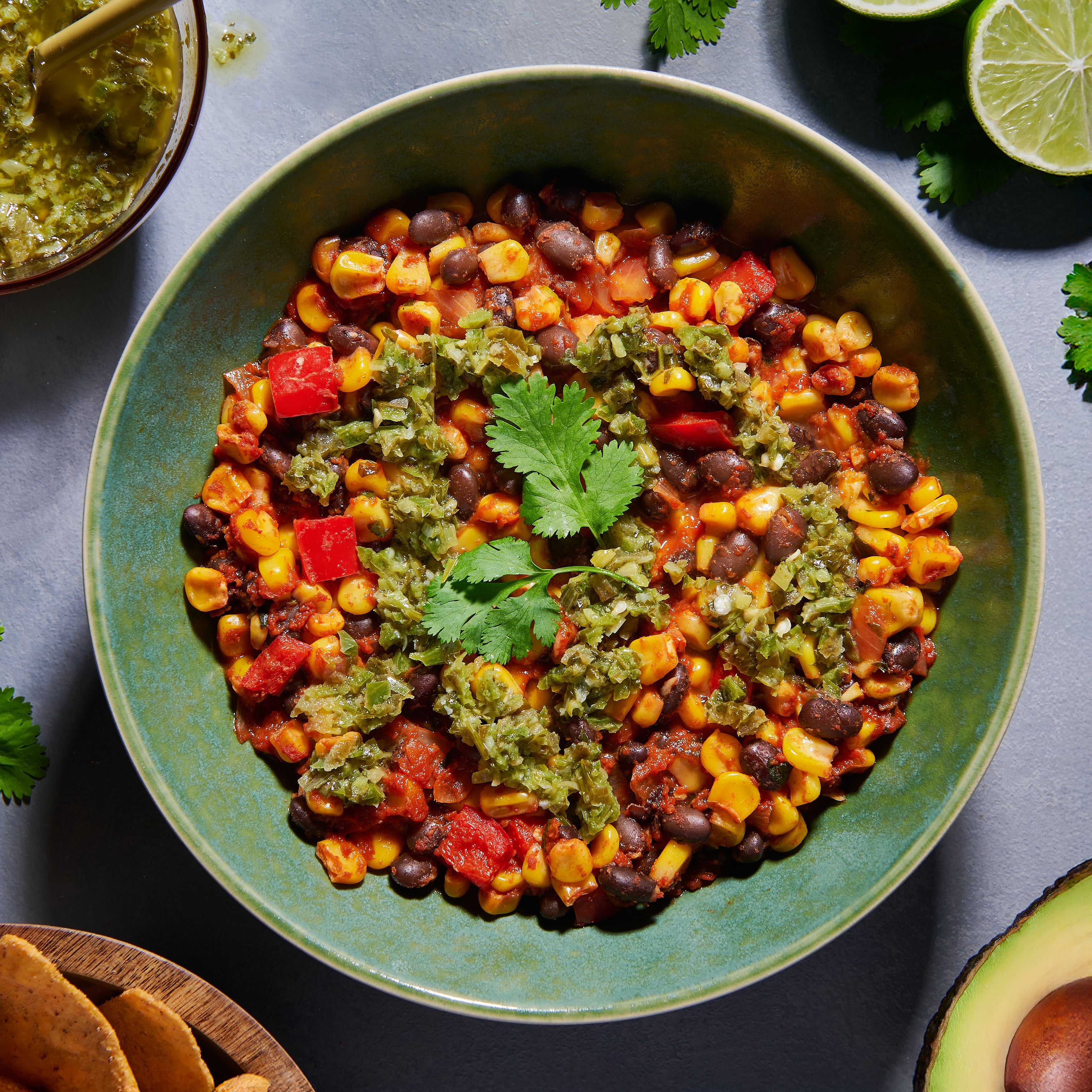Bowl of black beans with roast corn and jalapeño-lime salsa, topped with coriander, served with lime and avocado on the side.