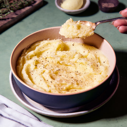 Bowl of fluffy buttered mashed potato, creamy and smooth with some black pepper to garnish, and a spoonful being scooped out