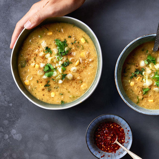 Bowl of chicken and sweet corn soup topped with spring onions, coriander, and cracked pepper, served with chili oil on the side.