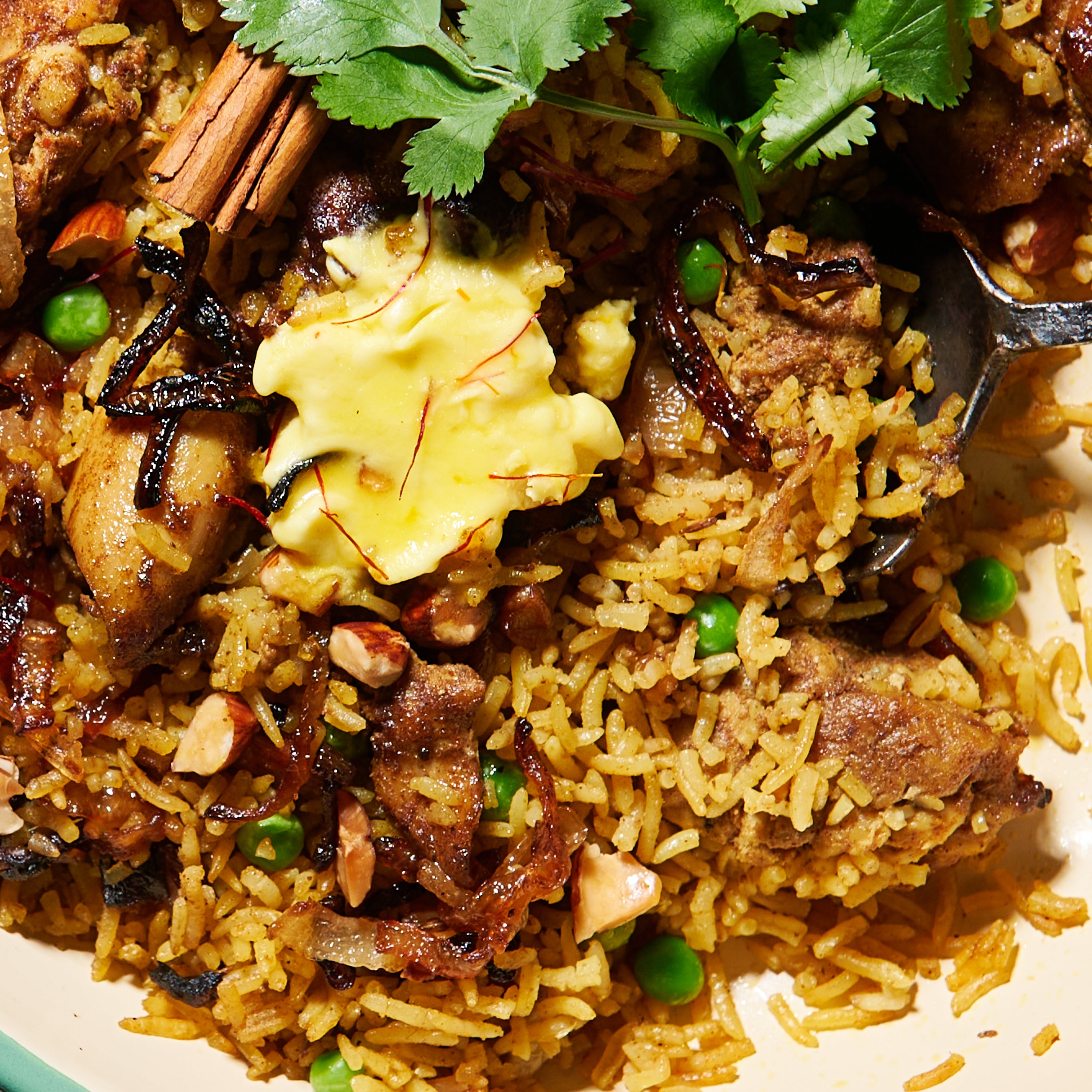 Close-up of saffron butter melting into spiced rice and chicken biryani, with peas, toasted nuts, and caramelised onions.