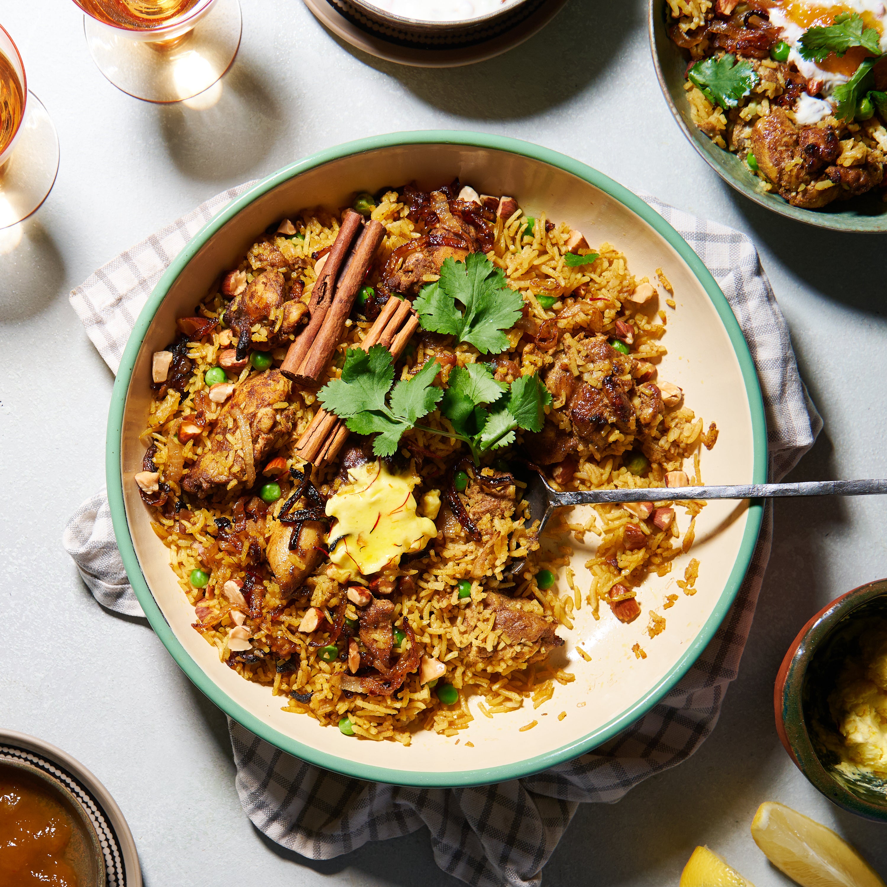 A large dish of chicken biryani with golden saffron rice, tender chicken pieces, peas, caramelised onions, toasted almonds, and whole cinnamon sticks, garnished with fresh coriander.