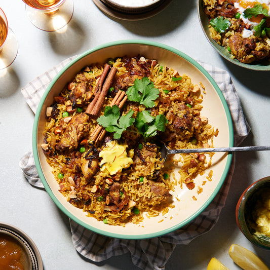 A large dish of chicken biryani with golden saffron rice, tender chicken pieces, peas, caramelised onions, toasted almonds, and whole cinnamon sticks, garnished with fresh coriander.