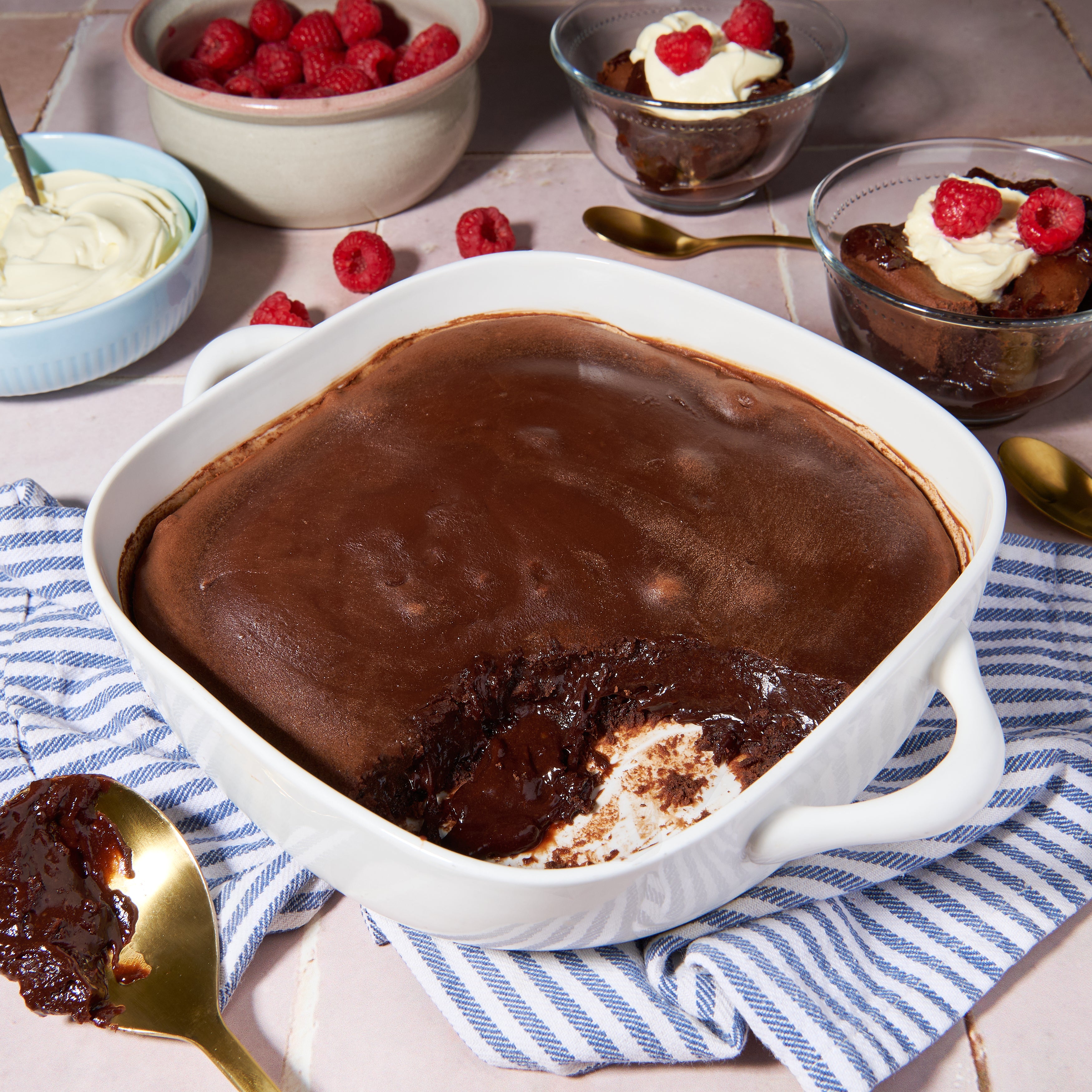 Chocolate lava cake served in a dish with bowls of cream and raspberries in the background.