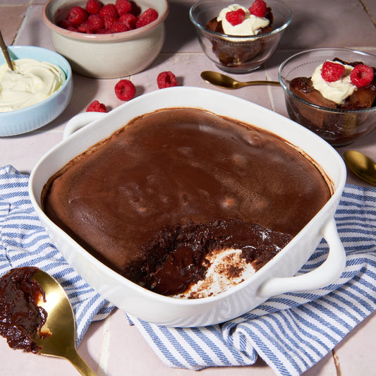 Chocolate lava cake served in a dish with bowls of cream and raspberries in the background.