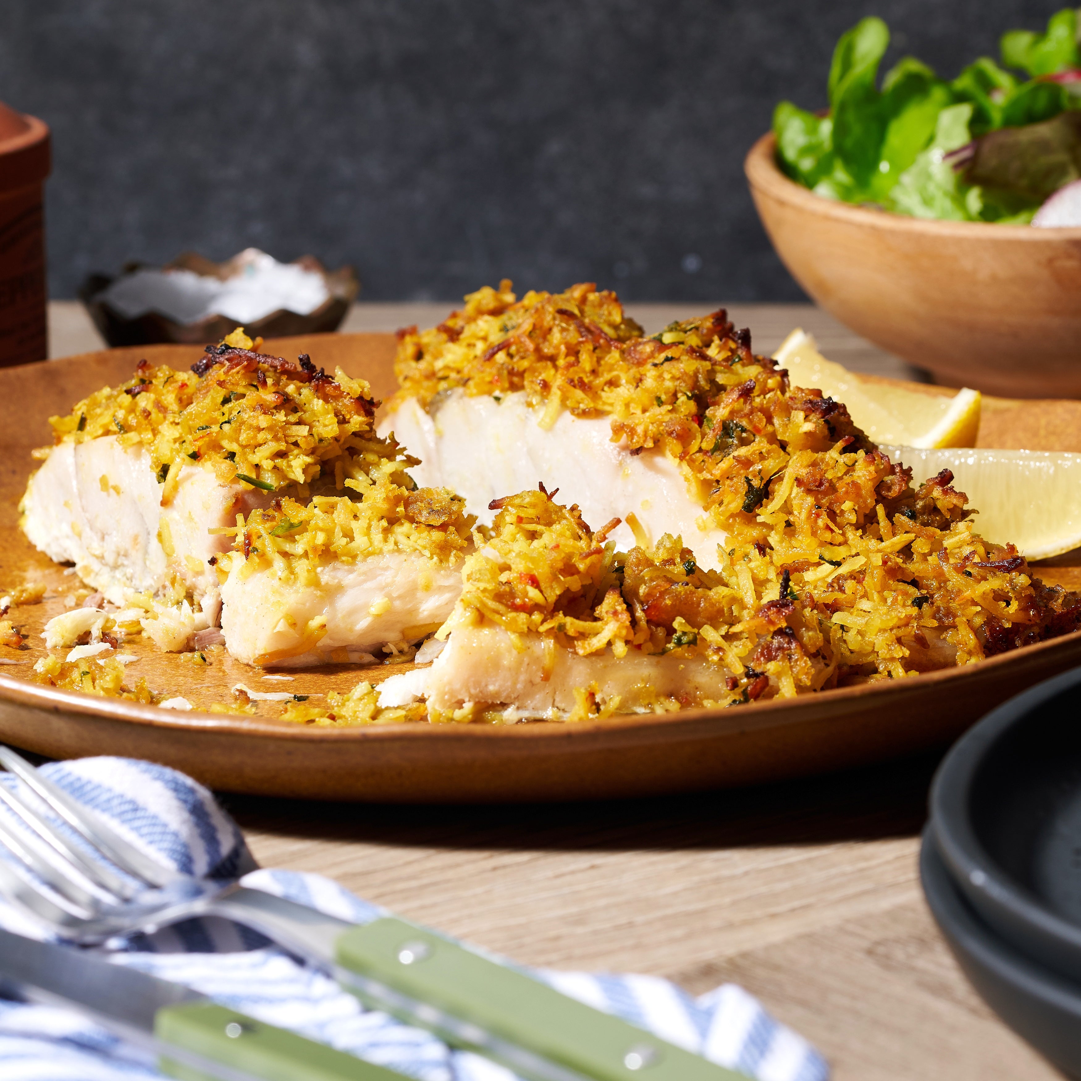 Humpty Doo barramundi fillet cut into pieces, topped with crunchy coconut crust, with lemon wedges and fresh salad on the side.