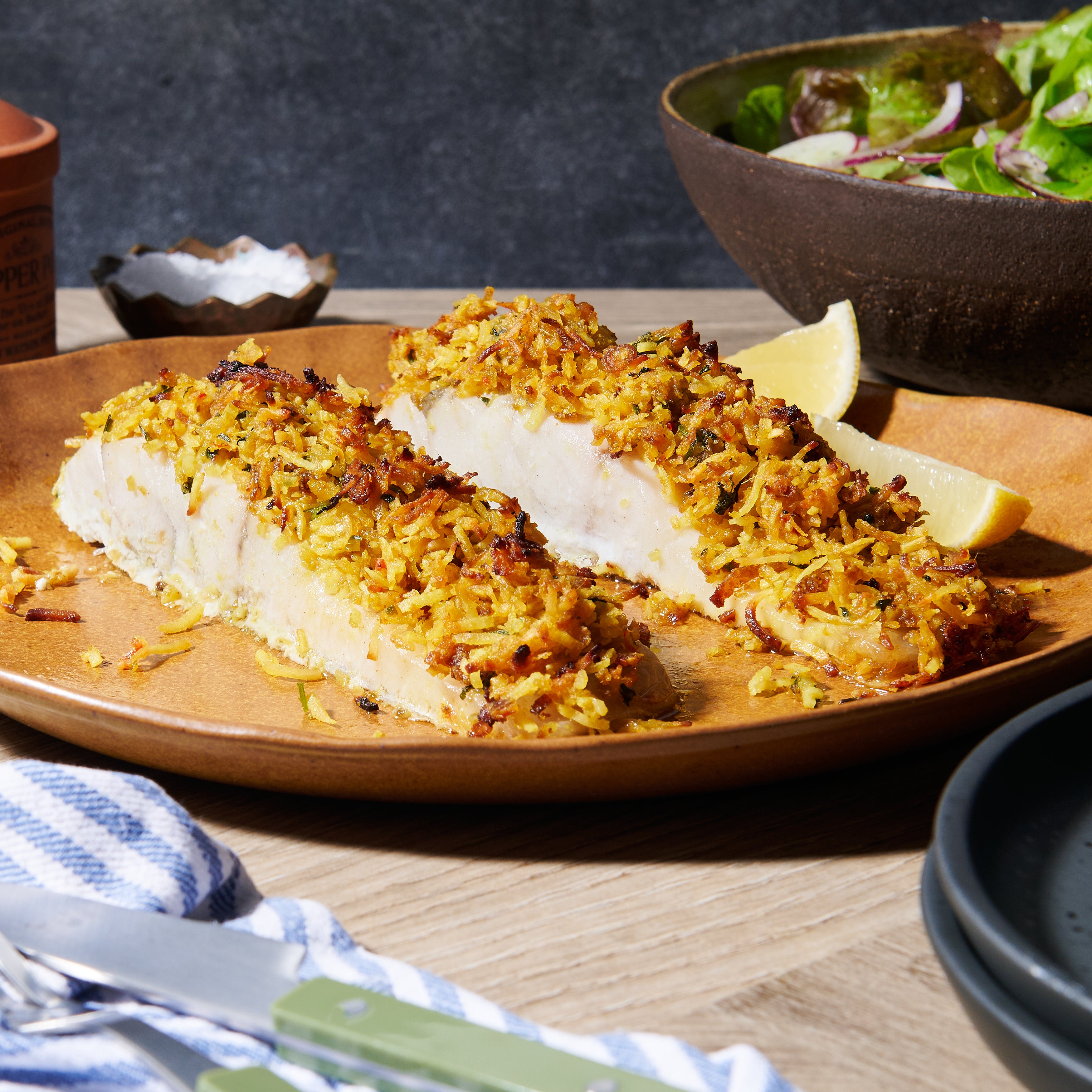 Plate of Coconut-Crusted Humpty Doo Barramundi fillets topped with golden coconut and chilli crust, served with lemon wedges and salad.