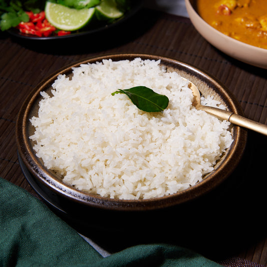 Steamed coconut white rice in a dark bowl garnished with a keffir lime leaf, served with a curry and fresh chilli and lime on the side