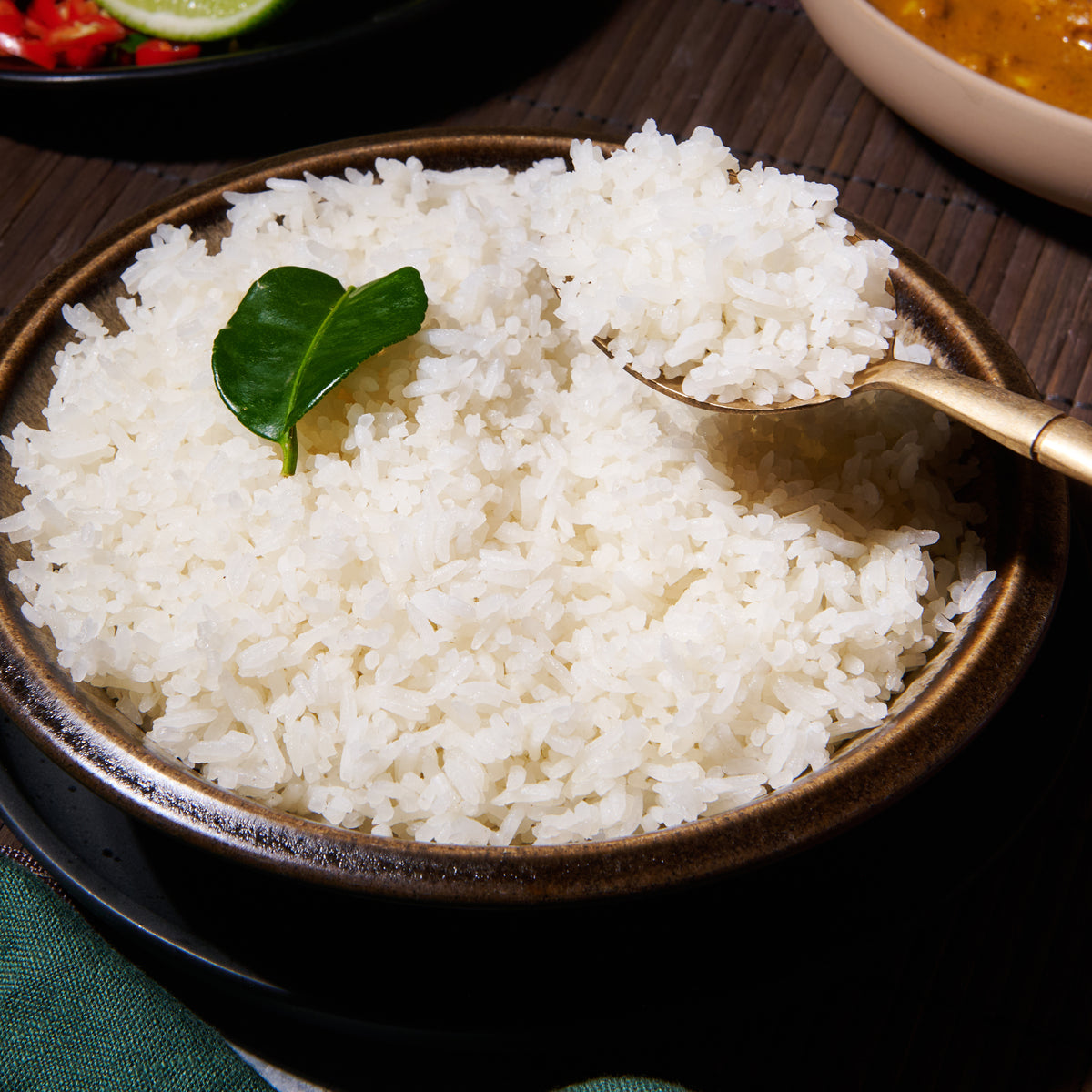 close up of coconut rice with a spoon full being scooped out. Garnished with keffir lime leaf