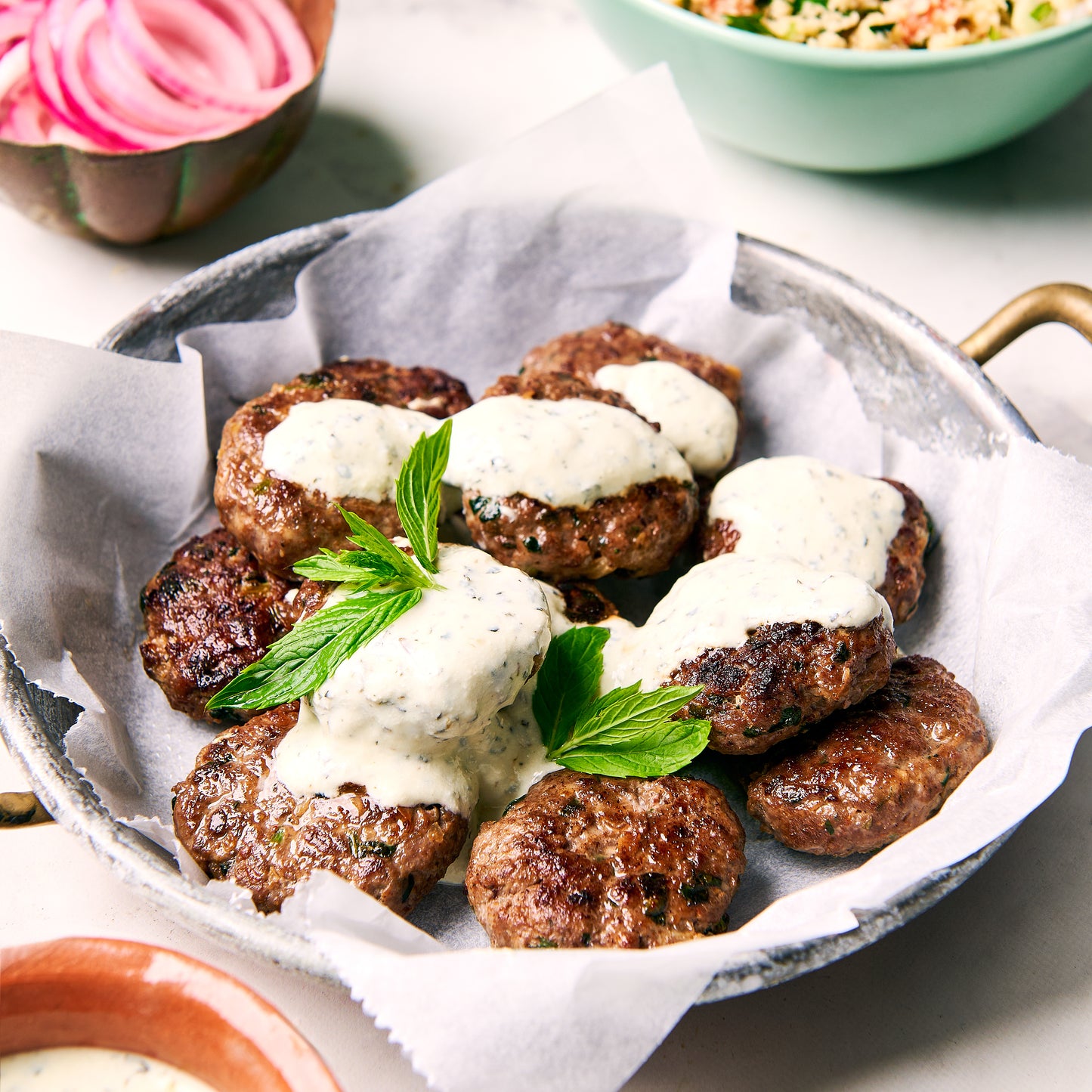 Dish of golden-brown lamb koftas, topped with creamy minted yoghurt and garnished with fresh mint leaves, ready to eat.
