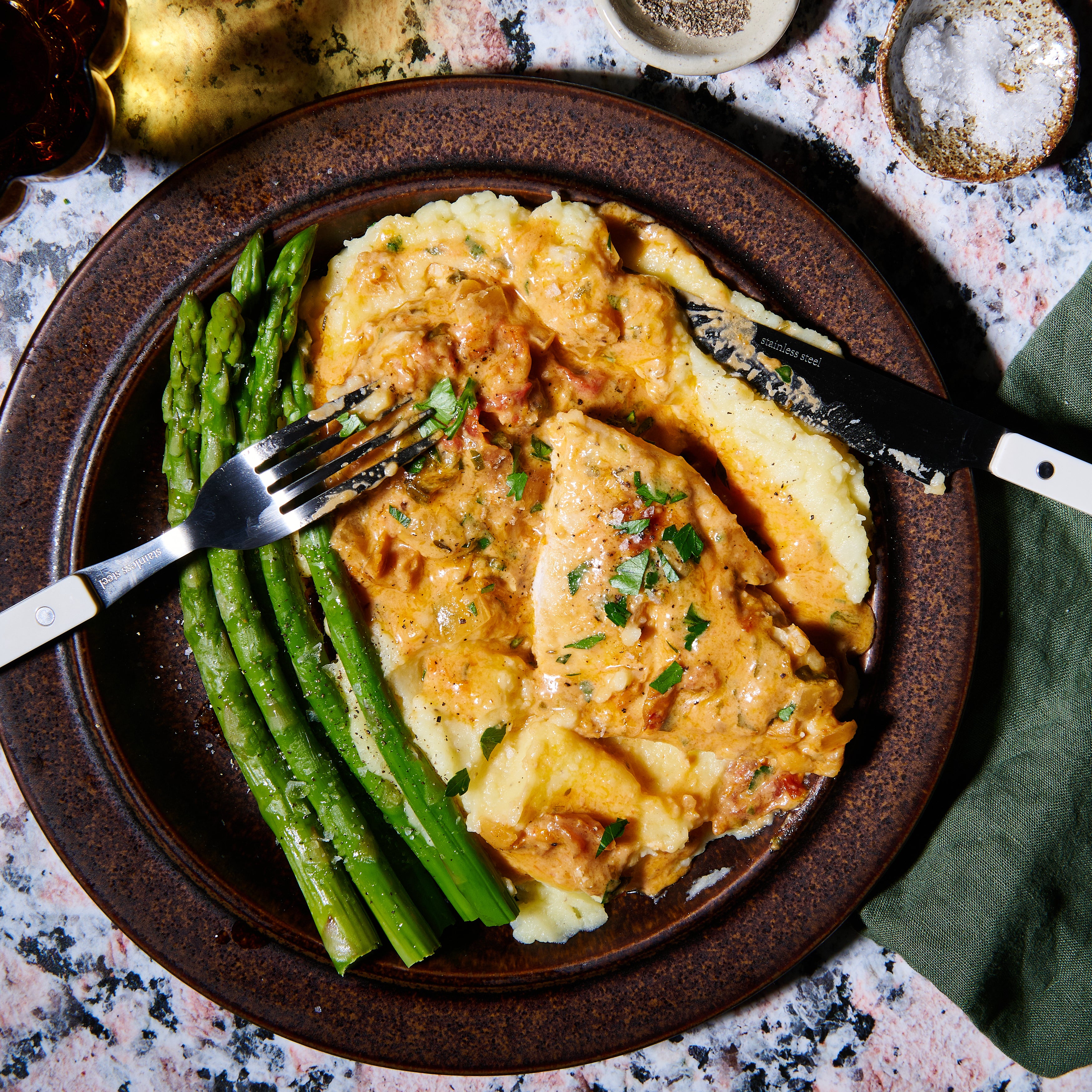 Plate of Marry Me Chicken with mashed potatoes and asparagus, covered in rich sun-dried tomato cream sauce.
