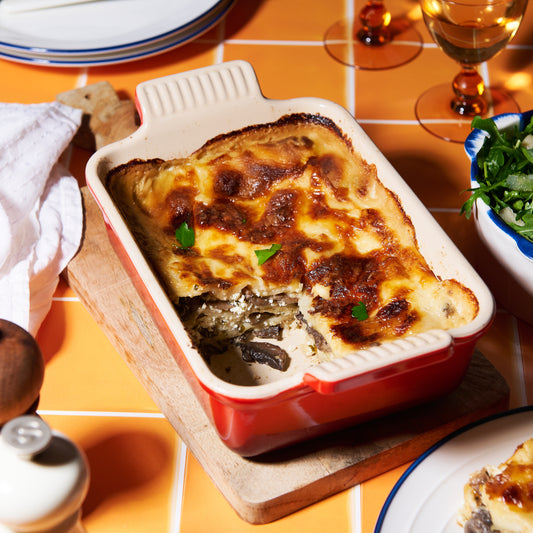 A golden-baked mushroom and ricotta lasagne in a red ceramic dish, with layers of creamy béchamel and melted mozzarella.