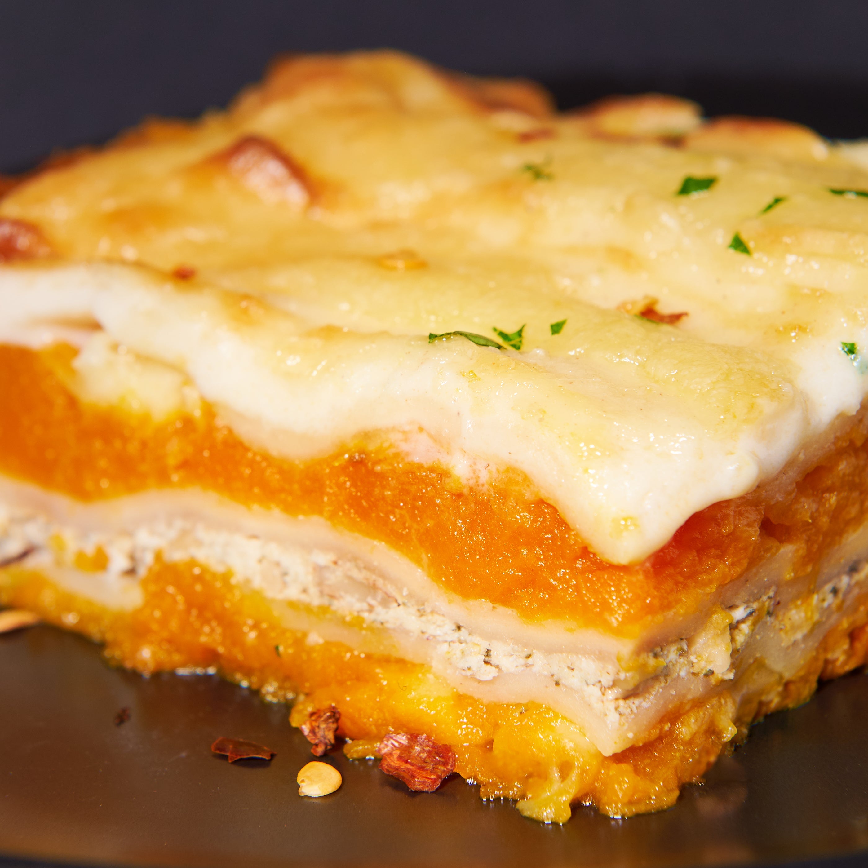 Close-up slice of pumpkin lasagne showing layers of roasted pumpkin, ricotta, and pasta under a cheesy topping.