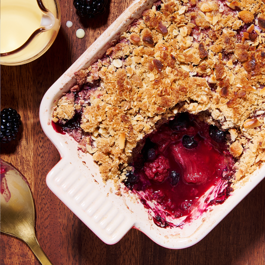 A golden crumble topped with oats and macadamias, baked over bubbling rhubarb and mixed berries in a white dish.
