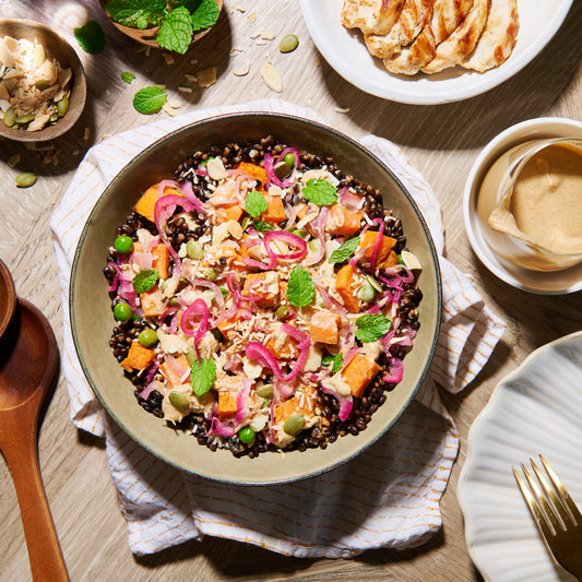 Bowl of roast sweet potato and black barley salad with peas, pickled onion, and fresh mint topped with creamy coconut dressing.