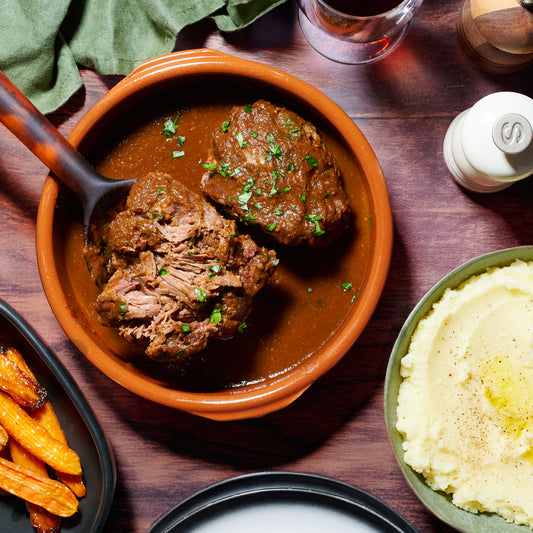 Overhead view of 10hr slow braised beef cheeks served in a terracotta bowl with rich sauce, mashed potatoes, and roasted carrots.