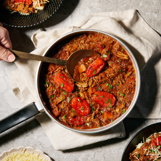 A pot of slow cooked lamb rags in rich tomato sauce with chunks of tender lamb and roasted roma tomatoes.