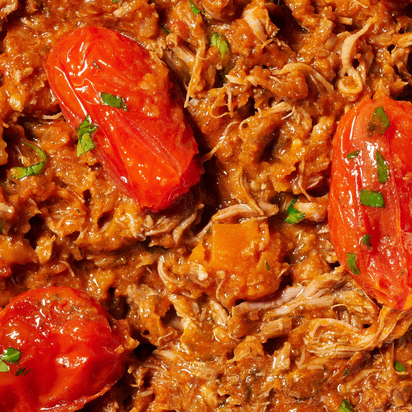 Close-up of shredded lamb in tomato-based sauce with sweet roasted roma tomatoes and herbs, showing its rich texture and flavour.