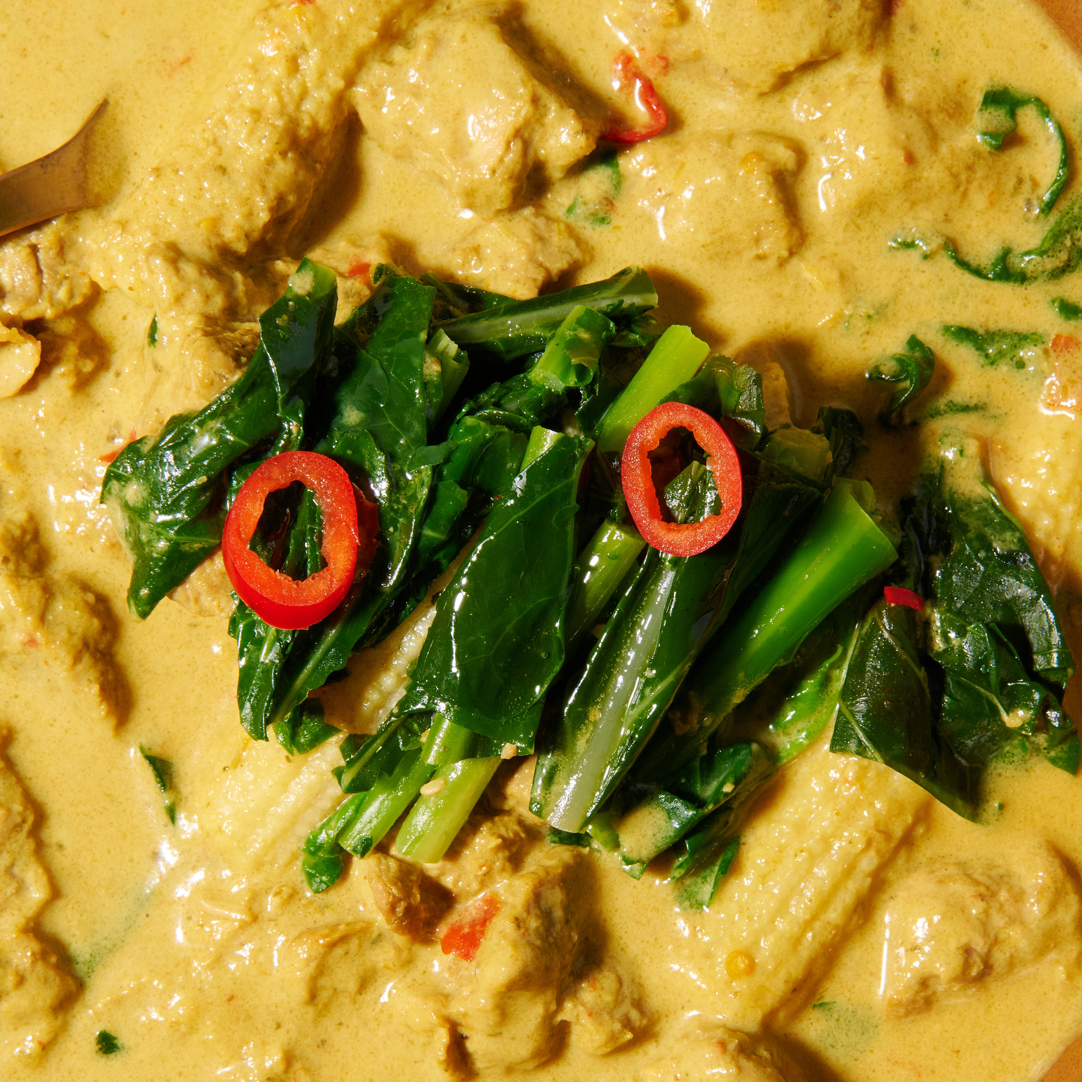 Close-up of Thai pork curry with tender pork, greens, and red chilli slices in golden coconut curry.