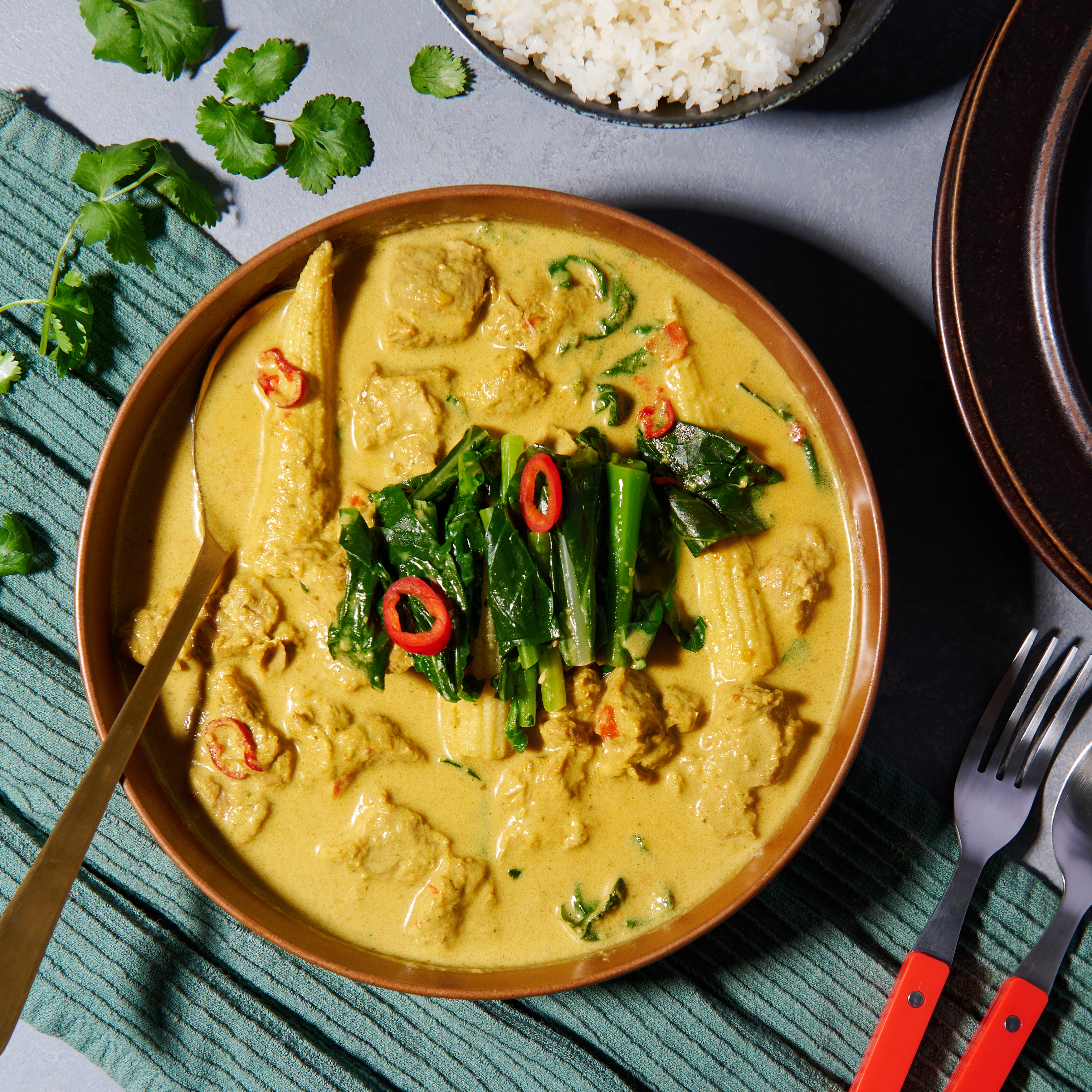 Bowl of Thai pork curry with lemongrass, ginger, baby corn, and Chinese broccoli in creamy coconut sauce.