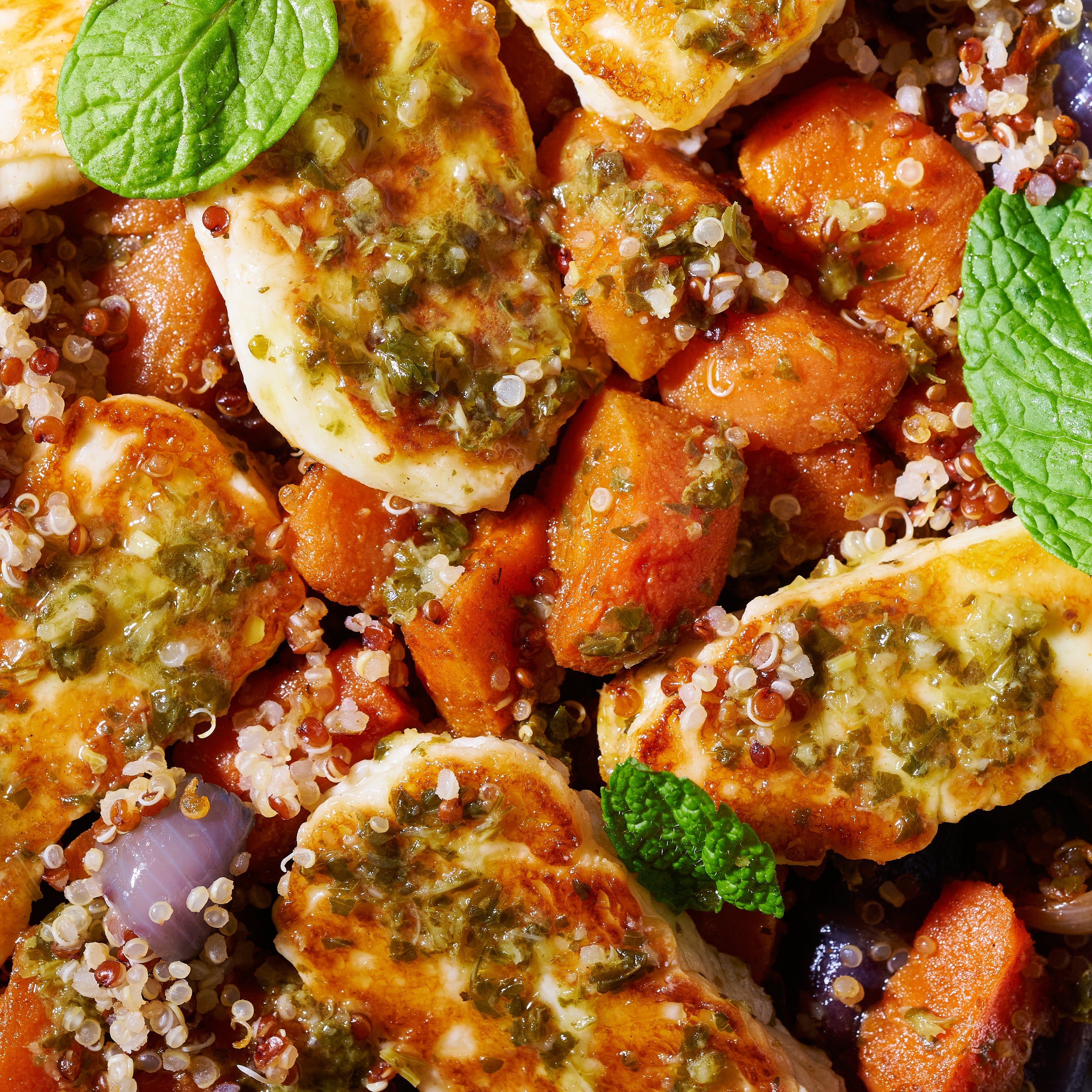 Close-up of caramelised roast carrots, fluffy quinoa, and seared halloumi topped with a tangy green herb dressing and scattered fresh mint.