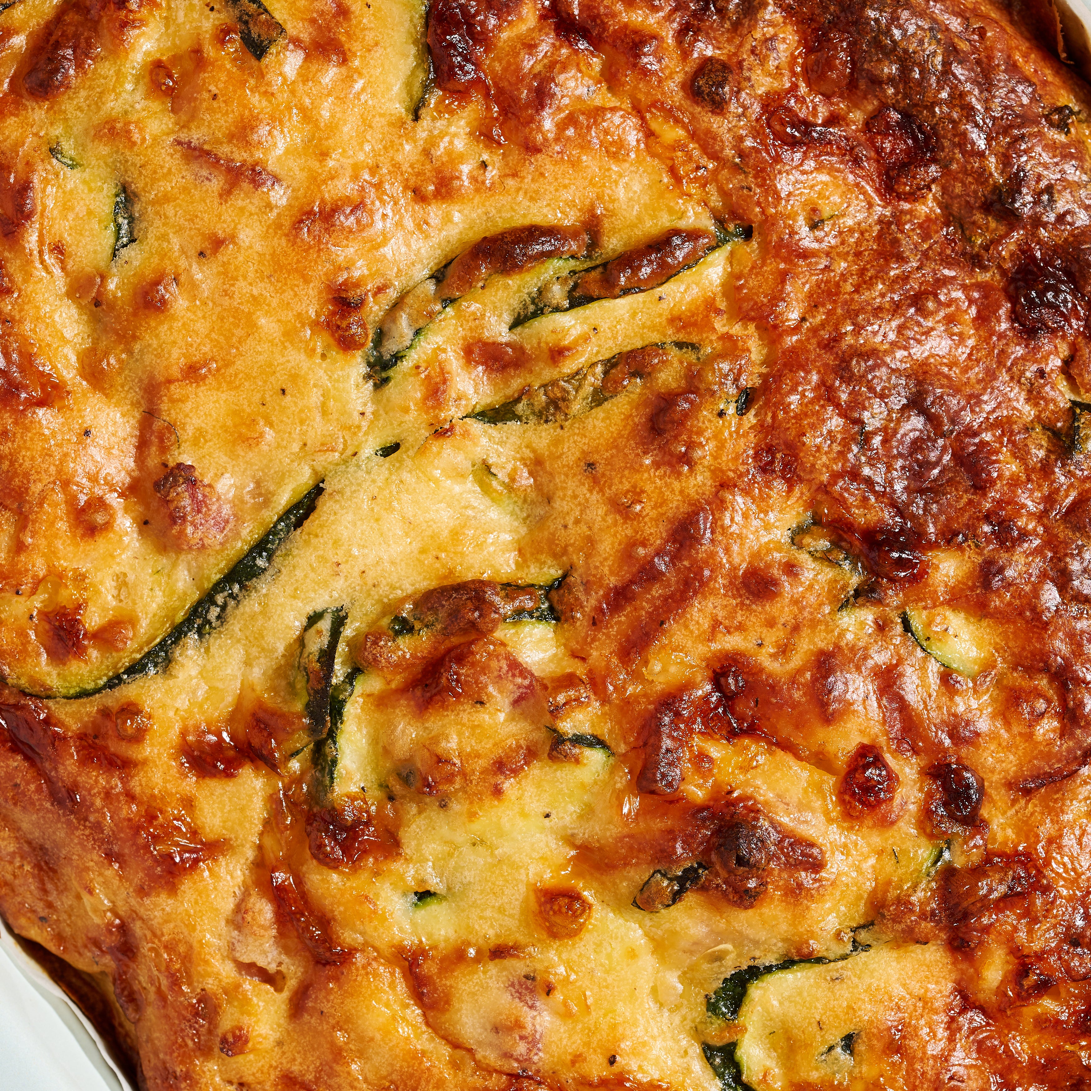 Close-up of cheesy zucchini and pancetta slice, showing golden crust and flecks of zucchini and pancetta throughout.