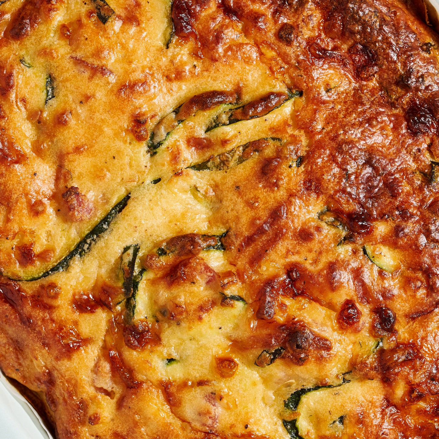 Close-up of cheesy zucchini and pancetta slice, showing golden crust and flecks of zucchini and pancetta throughout.