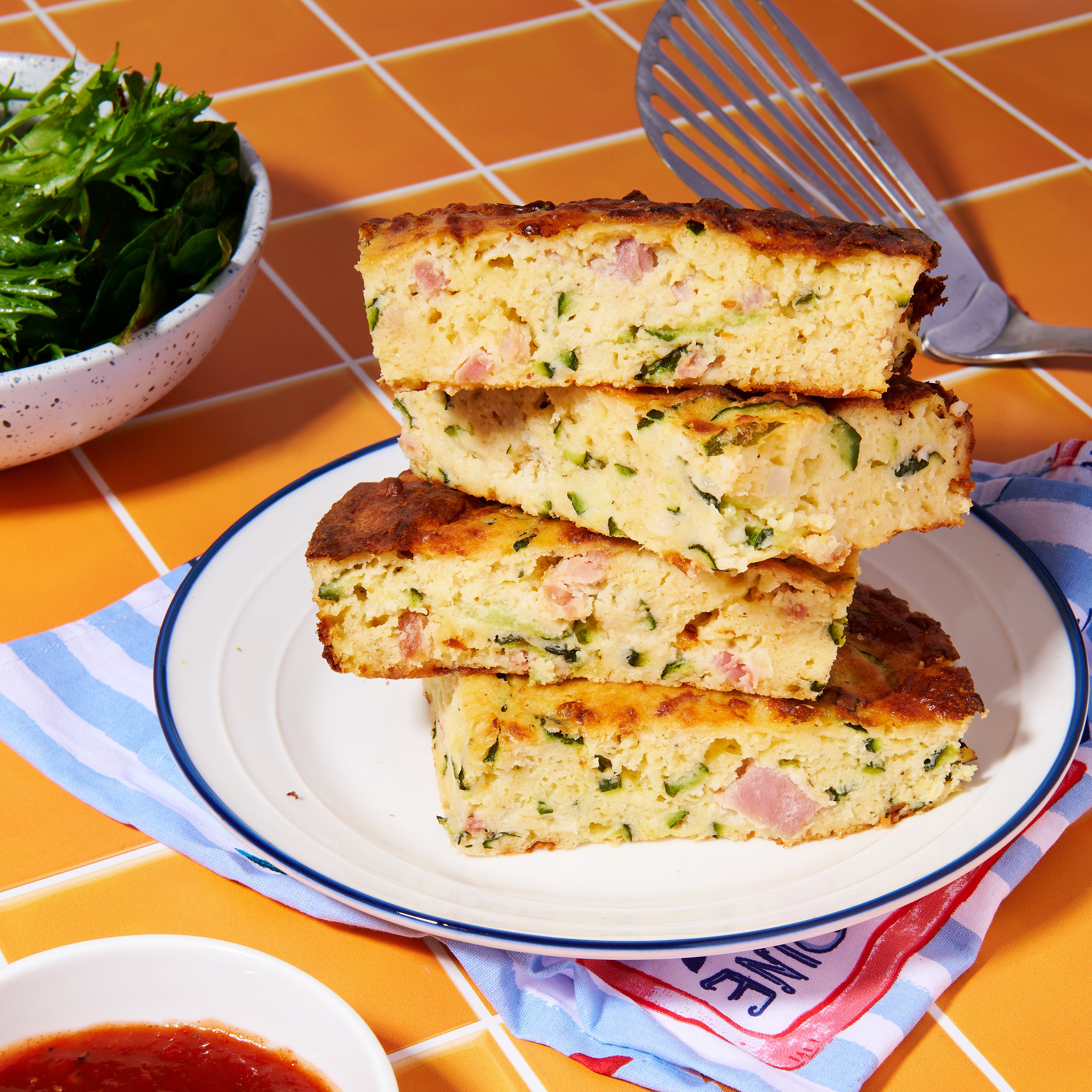 Thick wedges of zucchini and pancetta slice stacked on a plate, with a crisp golden crust and tender, cheesy filling inside.