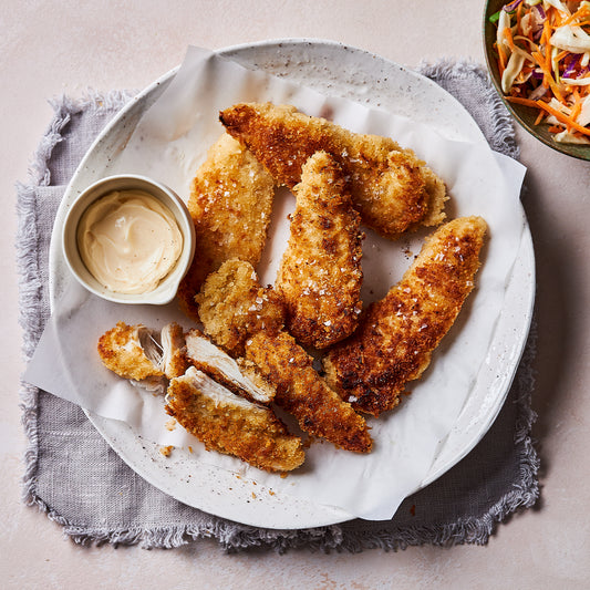 Plate of golden Crumbed Chicken Tenderloins with sea salt flakes, served with dipping sauce and a side of coleslaw.