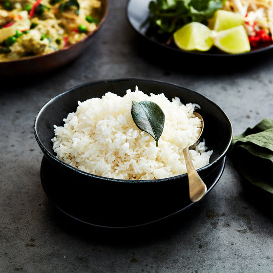 Bowl of fluffy coconut jasmine rice topped with a kaffir lime leaf and a spoon resting inside.