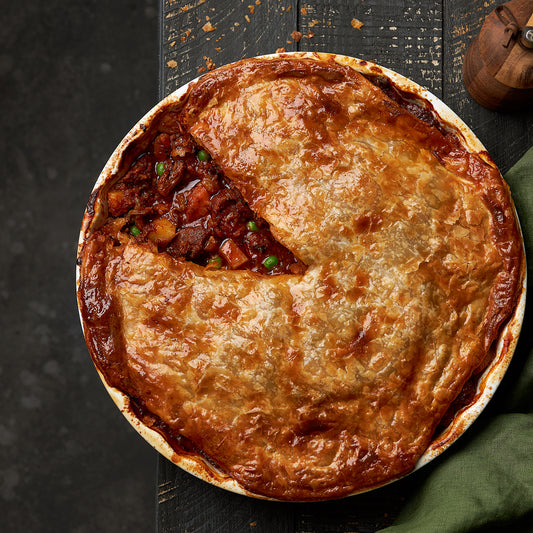 Overhead view of a family-sized beef and vegetable pie in a round baking dish with golden crust.